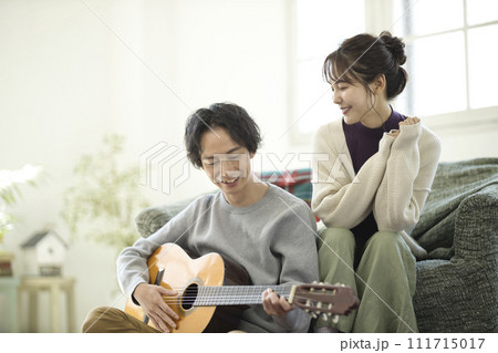 ソファーに座ってギターを弾きながら歌う若いカップル 111715017