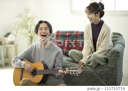 ソファーに座ってギターを弾きながら歌う若いカップル ソファーに座ってギターを弾きながら歌う若いカップル 111715719