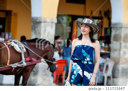 Beautiful woman wearing the traditional Colombian hat called Sombrero Vueltiao at the Carriage Square on the historical streets of Cartagena de Indias walled city 111715847