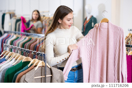 Dreamy female in casual outfit holding a pink buttonless jacket while shopping in a mall Dreamy female in casual outfit holding a pink buttonless jacket while shopping in a mall 111716206