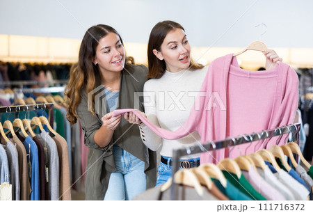 Cheerful female friends talking and chossing pink cardigan in a clothing store 111716372
