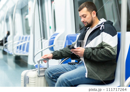 Bearded traveler sitting with suitcase and smartphone in metro car 111717264