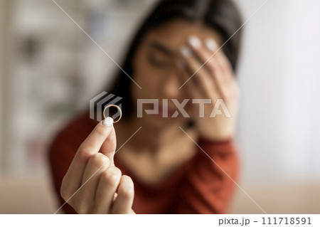 Upset young woman holding wedding ring in focus with pained expression 111718591