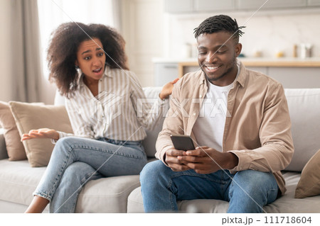 Discontented Black Wife Looking At Husband Browsing On Phone Indoor Discontented Black Wife Looking At Husband Browsing On Phone Indoor 111718604