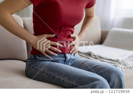 Unrecognizable woman experiencing abdominal pain at home 111719030