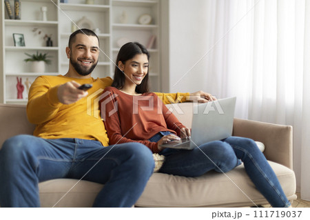 Couple Resting On Couch At Home, Man Watching Tv, Woman Using Laptop Couple Resting On Couch At Home, Man Watching Tv, Woman Using Laptop 111719037
