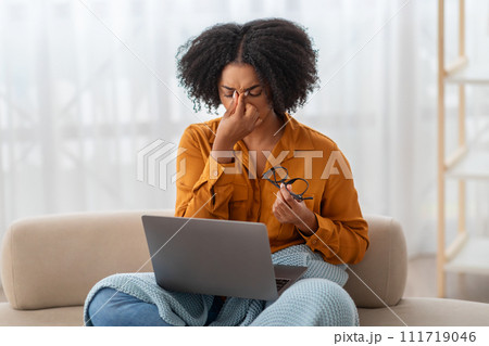 An overwhelmed African American woman with a laptop pinches the bridge of her nose An overwhelmed African American woman with a laptop pinches the bridge of her nose 111719046