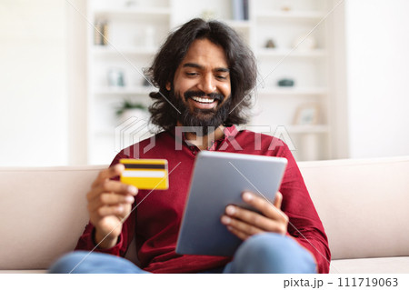 Happy indian guy banking from home, using tablet and card 111719063