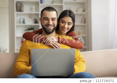 Happy young couple websurfing on laptop together while relaxing at home 111719372