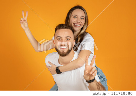 A joyful young couple poses playfully with the man carrying the woman on his back 111719390