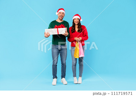 Happy Couple Holding Shopper Bags And Wrapped Present, Blue Background 111719571