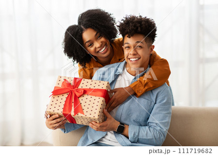 A cheerful young couple in casual attire shares a joyful moment while holding a large gift 111719682