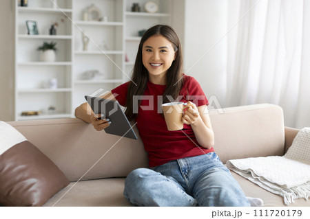 Relaxed asian woman holding cup of coffee and using digital tablet Relaxed asian woman holding cup of coffee and using digital tablet 111720179