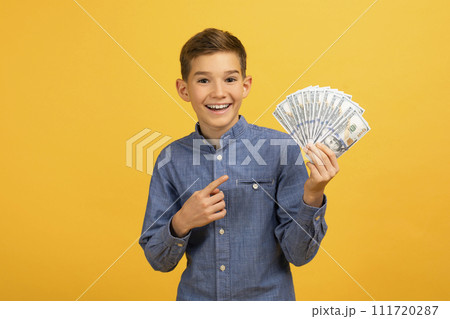 Cheerful teenage boy in denim shirt pointing at fan of dollar bills Cheerful teenage boy in denim shirt pointing at fan of dollar bills 111720287