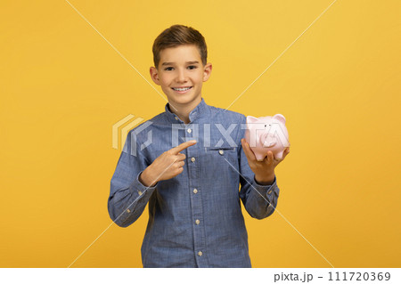 Happy excited teen boy pointing at piggy bank and looking at camera 111720369