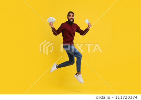 Excited millennial indian guy holding money cash in hands, jumping 111720374