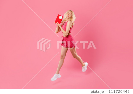 Blissful young woman leaping with joy, holding red gift box Blissful young woman leaping with joy, holding red gift box 111720443