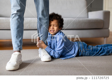 Upset child boy clinging to father's leg at home Upset child boy clinging to father's leg at home 111720725