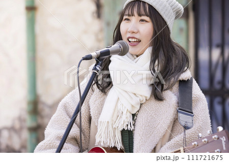 冬に弾き語りで路上ライブをする若い女性 111721675