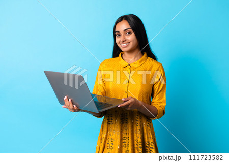 Happy middle eastern lady using laptop computer against blue backdrop Happy middle eastern lady using laptop computer against blue backdrop 111723582