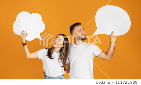 A man and woman holding blank speech bubbles overhead, looking at each other with smiles A man and woman holding blank speech bubbles overhead, looking at each other with smiles 111723589