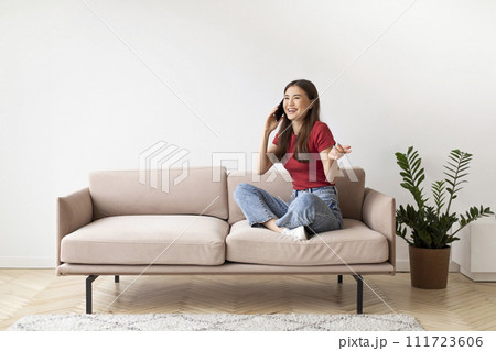 Cheerful young asian woman laughing joyfully while talking on cellphone at home 111723606