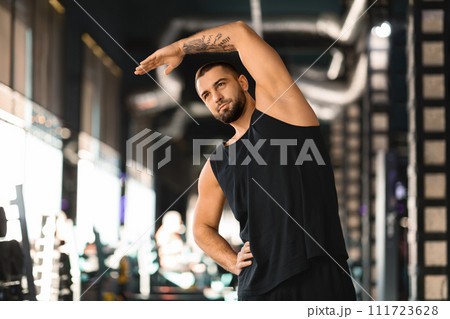 Handsome muscular man stretching his muscles before workout at modern gym Handsome muscular man stretching his muscles before workout at modern gym 111723628