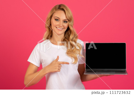 Happy blonde woman pointing at laptop with empty screen, studio Happy blonde woman pointing at laptop with empty screen, studio 111723632