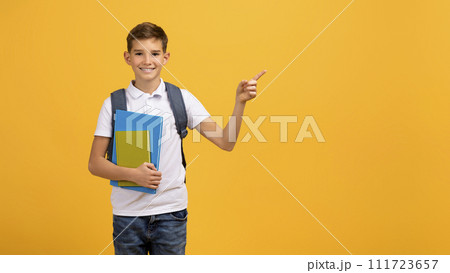 Happy schoolboy carrying backpack and textbooks and pointing aside at copy space Happy schoolboy carrying backpack and textbooks and pointing aside at copy space 111723657