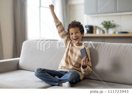 Little Black Boy Playing Games On Smartphone At Home And Celebrating Success 111723943