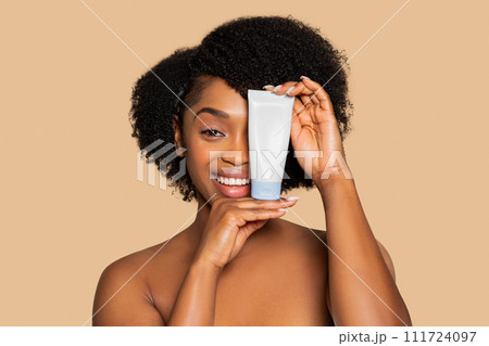 Smiling black woman holding skincare tube beside her face, mockup 111724097