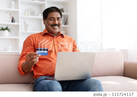 Mature indian man using laptop and credit card at home Mature indian man using laptop and credit card at home 111724117