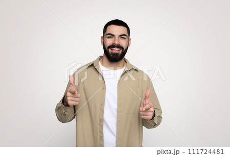 Glad confident handsome young latin man with a beard in casual point fingers at camera 111724481
