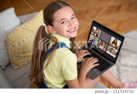 Smiling girl pupil sitting on couch at home, using laptop 111724710