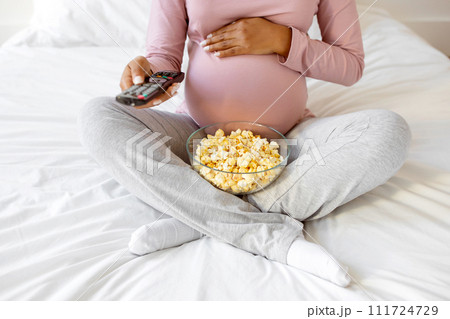 Cropped Shot Of Pregnant Woman With Popcorn And Remote Controller In Hands Cropped Shot Of Pregnant Woman With Popcorn And Remote Controller In Hands 111724729