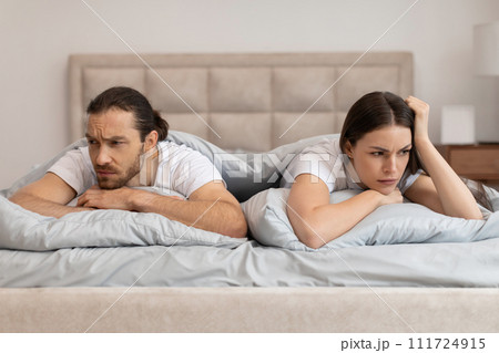 Couple in bed with worried expressions facing away 111724915