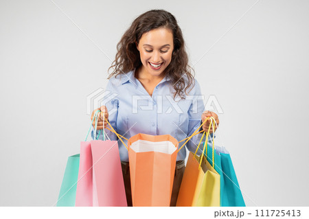 An exuberant young woman with curly hair, clad in a blue shirt, looks down 111725413