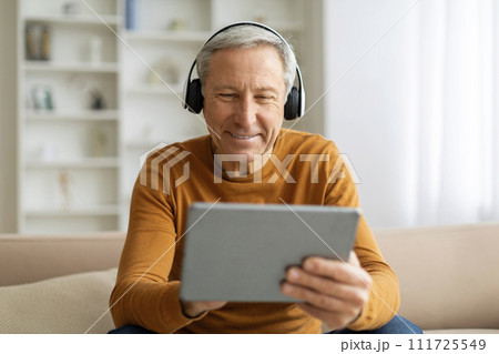 Positive elderly man using digital tablet and headphones at home Positive elderly man using digital tablet and headphones at home 111725549
