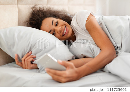 Cheerful Black Young Woman Using Smartphone Websurfing In Bed Indoor 111725601