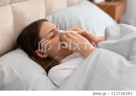 Young woman with cold, blowing her nose, lying in bed Young woman with cold, blowing her nose, lying in bed 111726361
