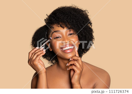 Happy african american woman applying eyeshadow, doing nude makeup Happy african american woman applying eyeshadow, doing nude makeup 111726374