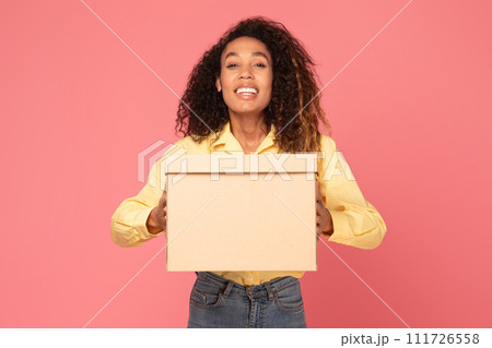 Young black woman smiles holding parcel on pink backdrop Young black woman smiles holding parcel on pink backdrop 111726558