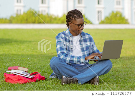 Smiling African American guy seated with laptop in park 111726577