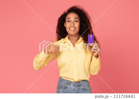 Happy black woman with credit card gesturing thumbs up on pink backdrop 111726681