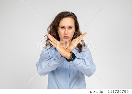 A determined young woman in a blue shirt makes an X sign with her arms A determined young woman in a blue shirt makes an X sign with her arms 111726796
