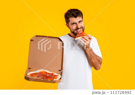 Caucasian man savoring slice of pizza from delivery box, studio Caucasian man savoring slice of pizza from delivery box, studio 111726992