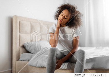 Tired african american millennial woman touching aching neck in bedroom 111727108