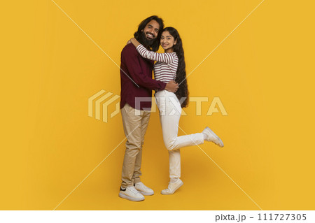 Loving millennial indian couple cuddling on yellow background 111727305