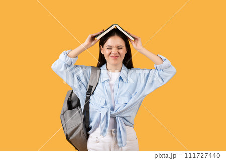 Tired female student with book on head and backpack Tired female student with book on head and backpack 111727440