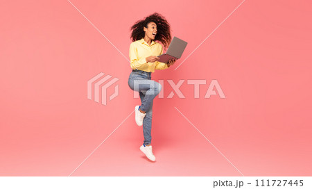 Excited black woman jumps, holding laptop on pink background 111727445